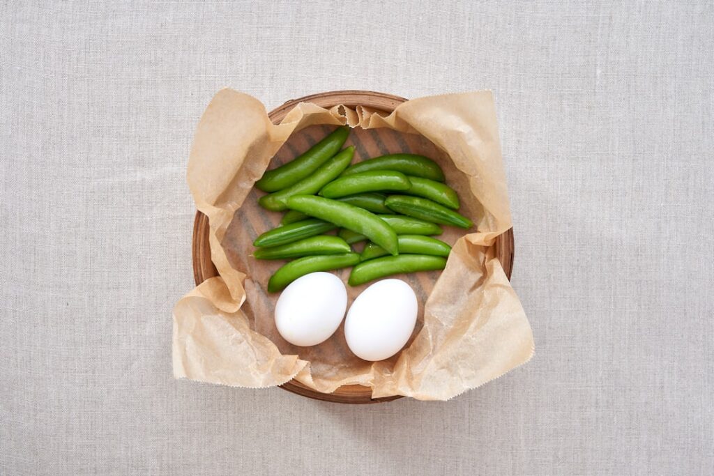 A bento-style box or small container filled with perfectly peeled hard-boiled eggs and vibrant green edamame pods ready 