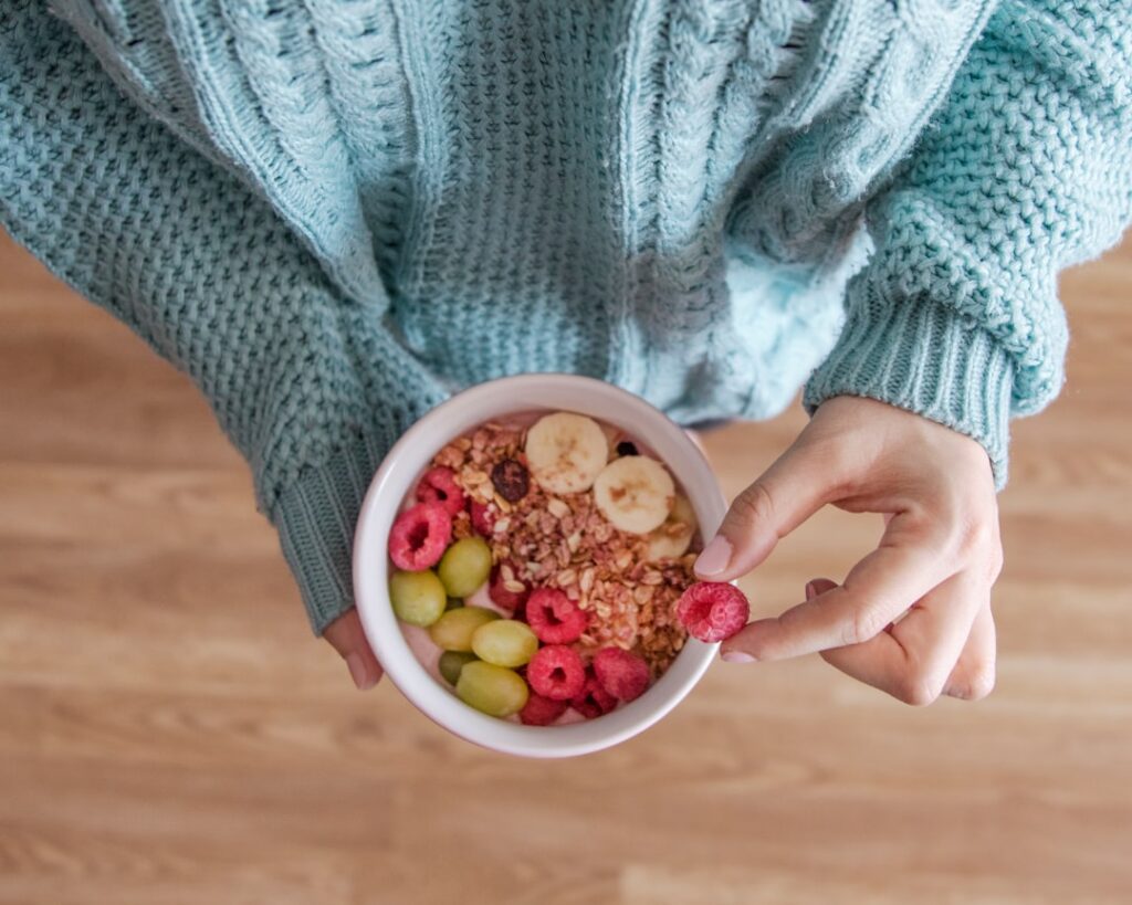 A person s hands holding a colorful bowl of fresh fruit and nuts symbolizing a healthy snack replacement The focus is on