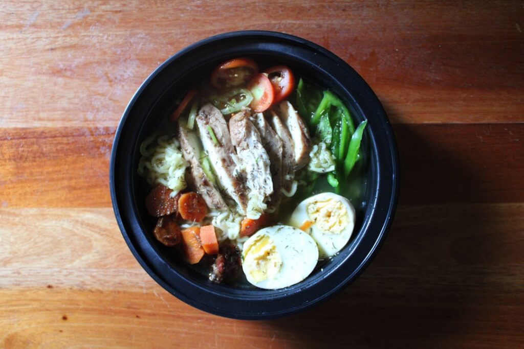 A close-up Pinterest-friendly image of a vibrant fresh high-protein chicken salad in a clear glass meal prep container w