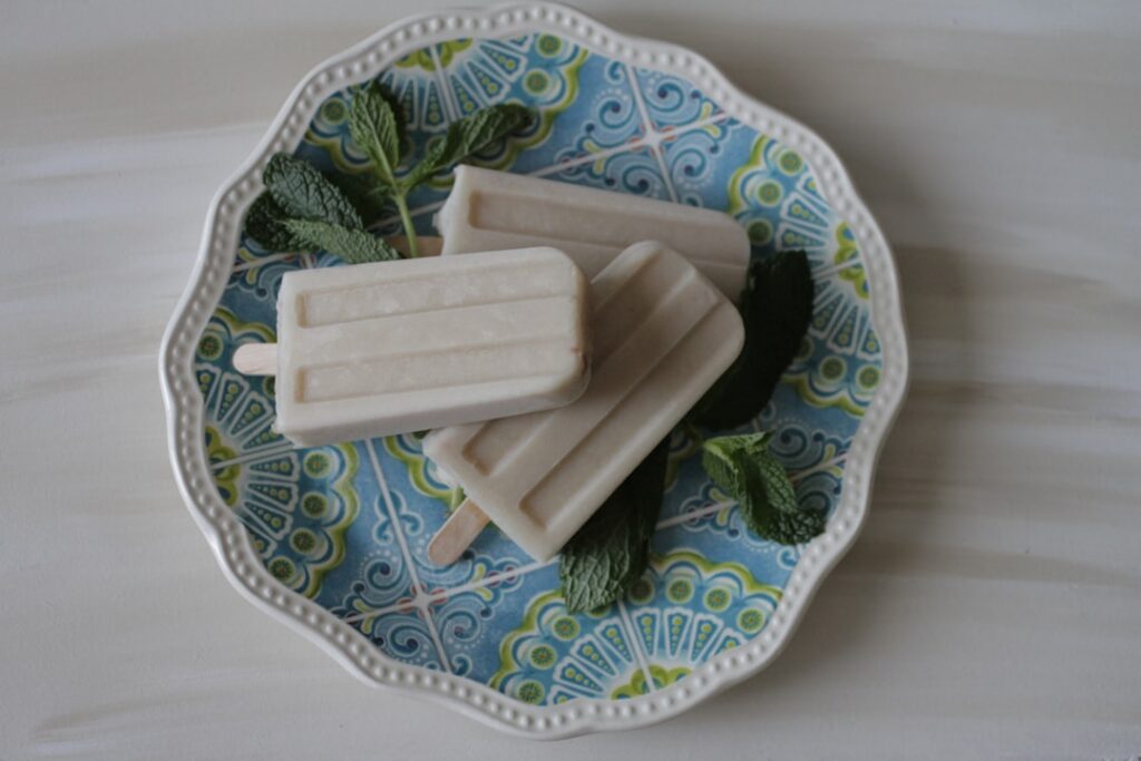 Elegant minimalist image of creamy pistachio pudding pops light green hue garnished with a few crushed pistachios on a c