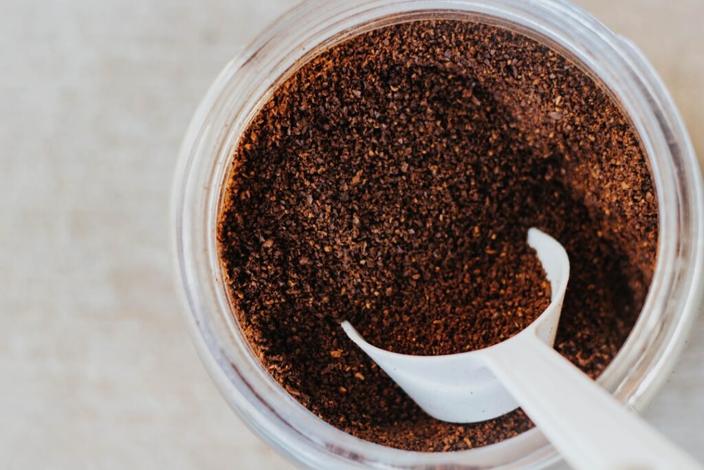 A close-up of dark rich coffee grounds in a small bowl with a rustic wooden spoon beside it suggesting natural ingredien