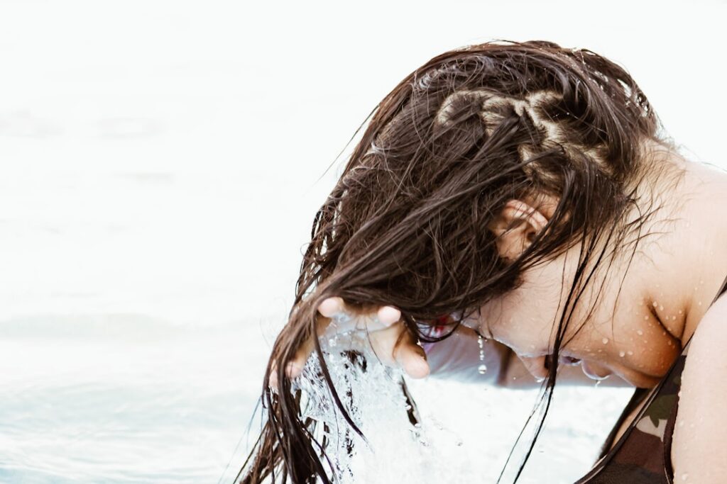 A close-up of a woman rinsing her hair with a bowl of cloudy rice water showing her long dark hair flowing under the gen