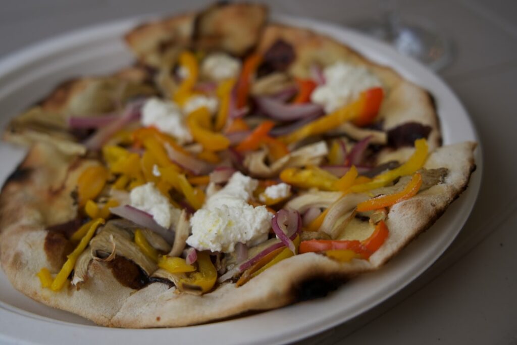 A savory cottage cheese flatbread topped with colorful vegetables like bell peppers onions spinach and cherry tomatoes f