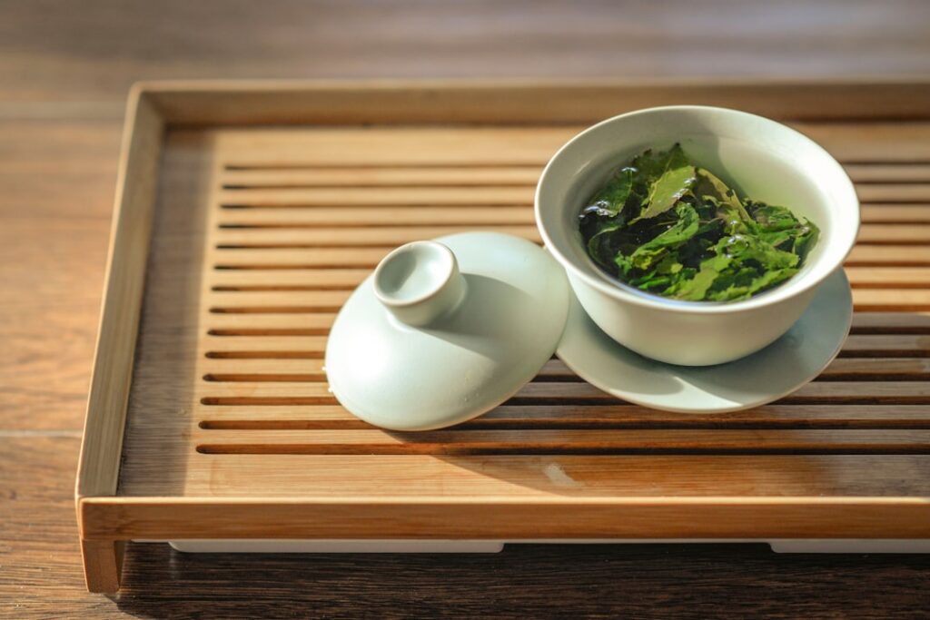 A beautifully composed serene image of a steaming cup of green tea on a minimalist wooden tray perhaps with a small cera