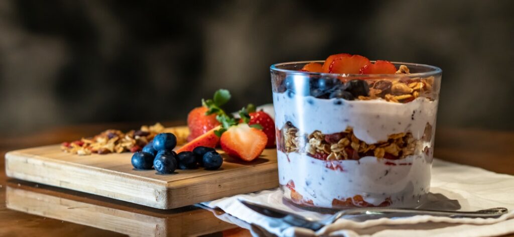 A vibrant modern wellness aesthetic photo of a layered yogurt parfait in a clear glass jar It shows creamy white yogurt 
