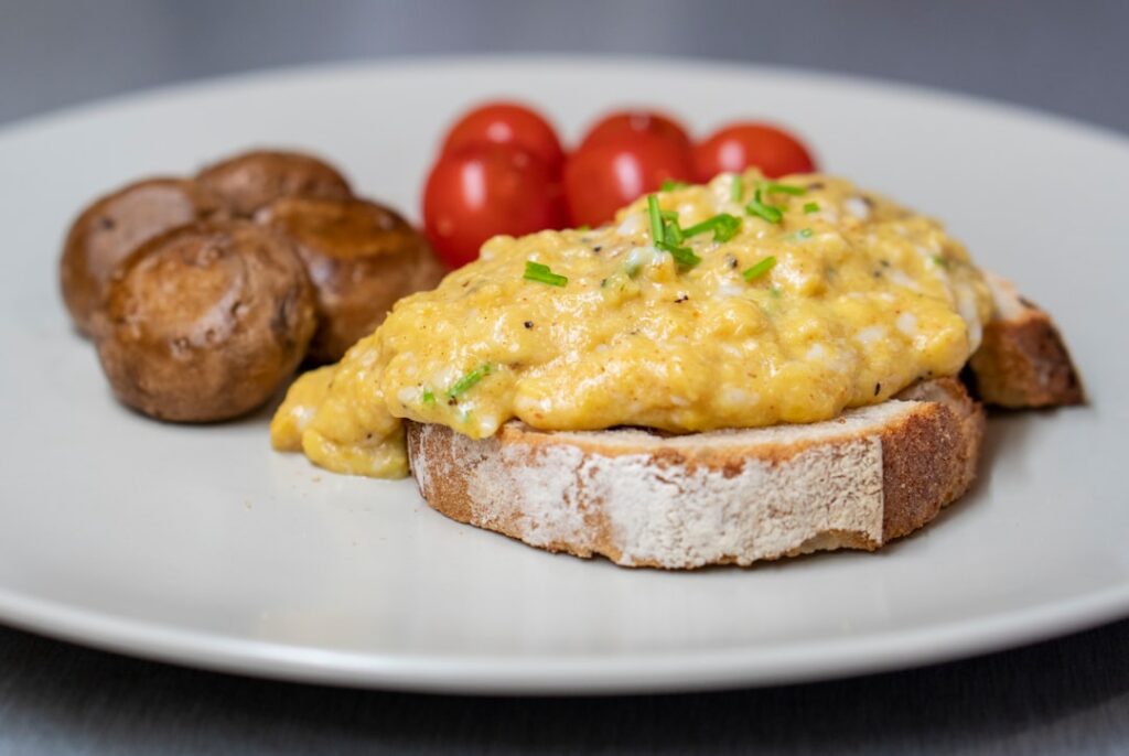 A vibrant and inviting veggie and feta egg scramble served with a slice of golden whole-grain toast on a clean white pla