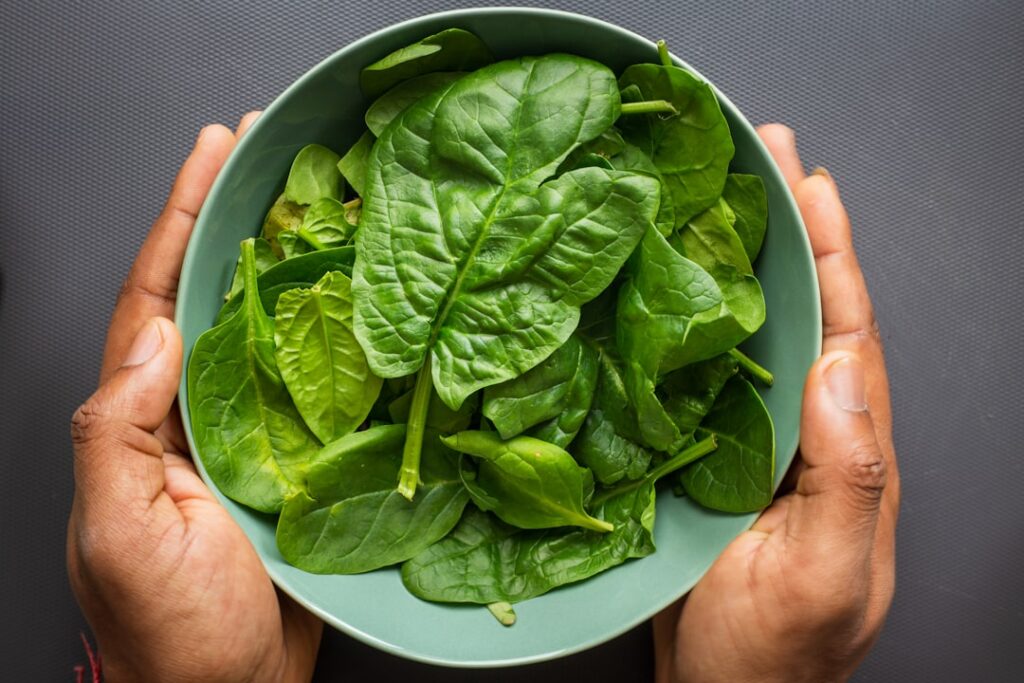 A vibrant bowl of fresh spinach leaves possibly with a few other salad ingredients like cherry tomatoes or cucumber slic