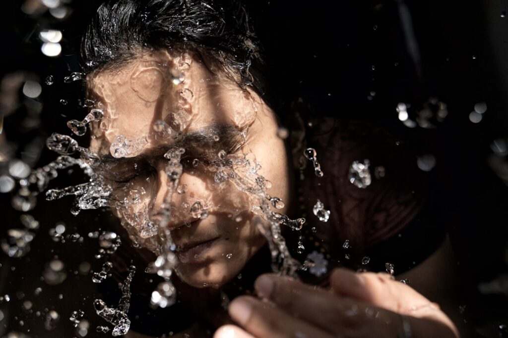 A woman gently rinsing her face with water after removing a face mask with a subtle healthy glow on her skin