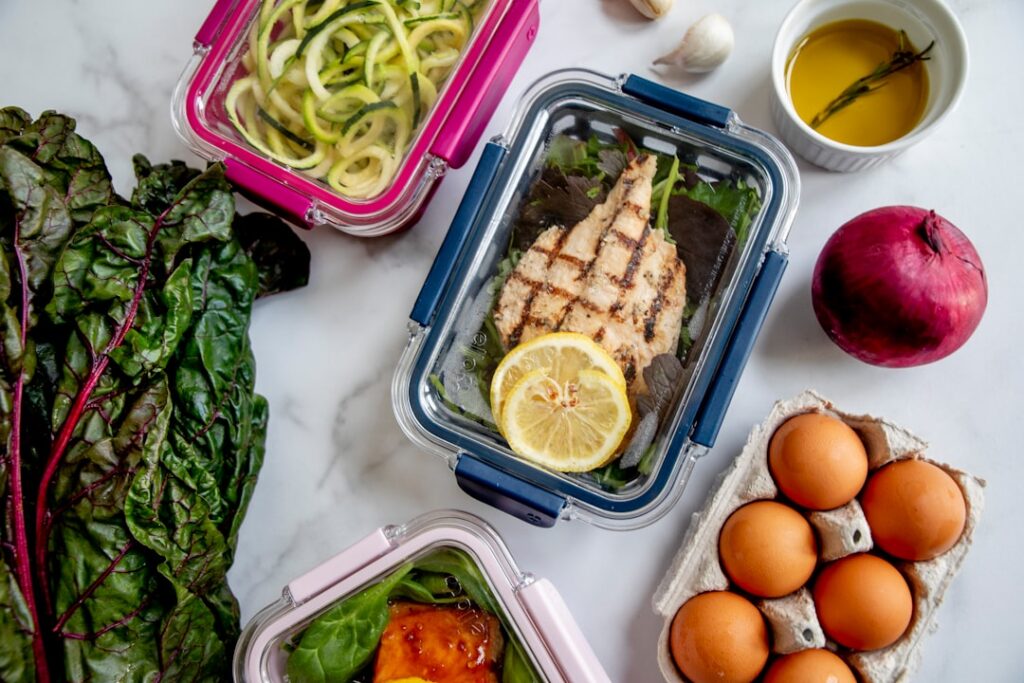 A variety of colorful prepped meal components arranged in separate glass containers and on a cutting board ready for ass