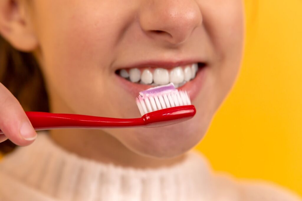 A person gently brushing their teeth with a dark charcoal paste on a toothbrush demonstrating the application process