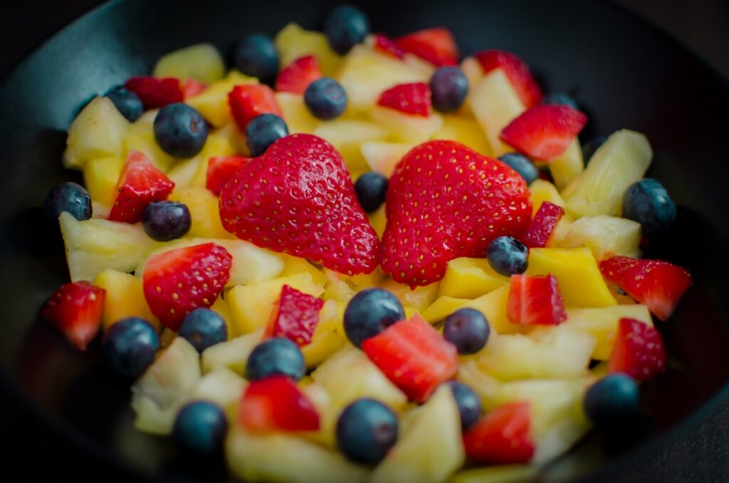 A close-up shot of a vibrant freshly prepared fruit salad in a clear glass bowl showcasing a mix of colorful fruits like