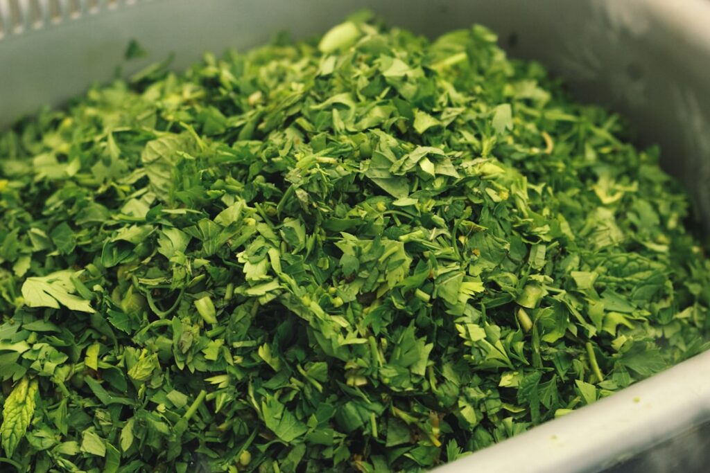 Chopped dried alfalfa leaves and a finer powder on a wooden cutting board next to an empty glass jar showing the process