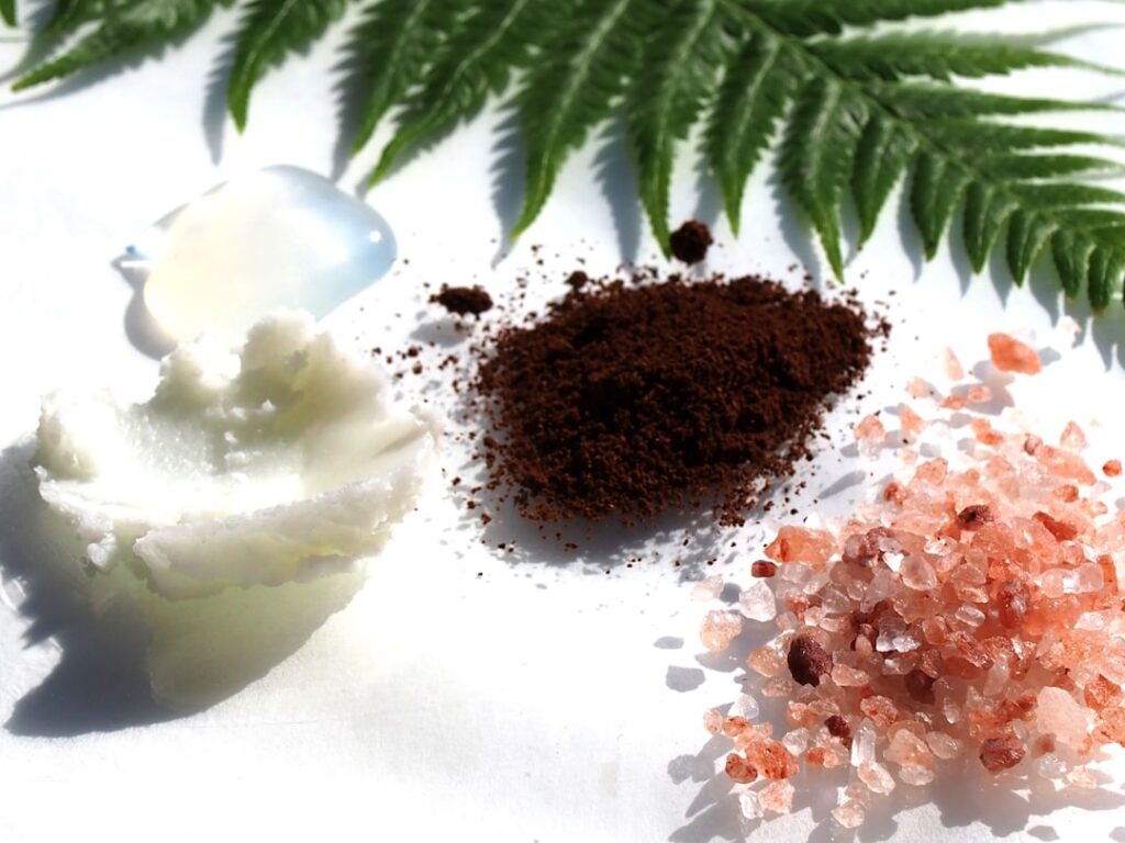 A small bowl filled with coffee grounds brown sugar and melted coconut oil being mixed with a spoon suggesting an invigo