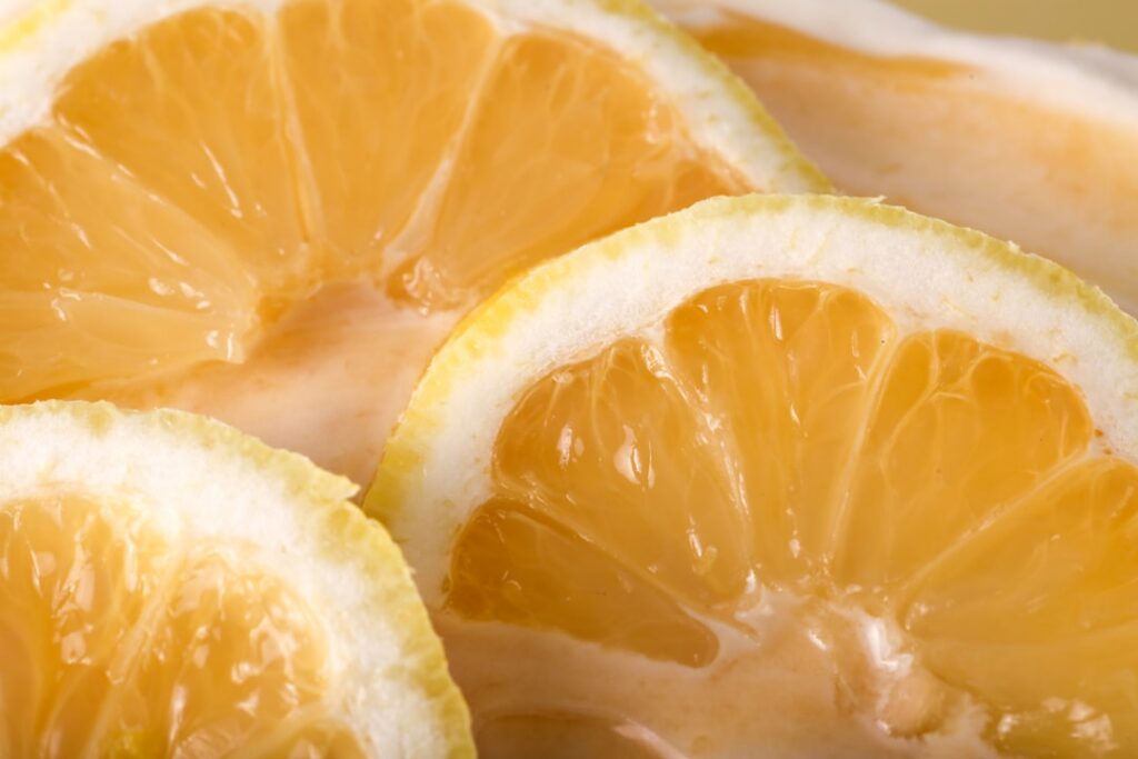 Close-up shot of a glass bowl of golden honey with a wooden dipper and several fresh yellow lemons some whole and some s