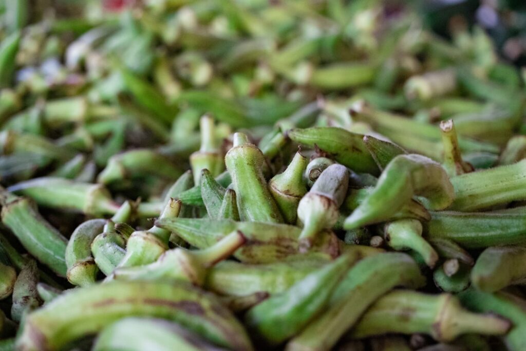 Close-up of fresh green okra pods and whole dried cloves artfully arranged on a rustic wooden surface highlighting their