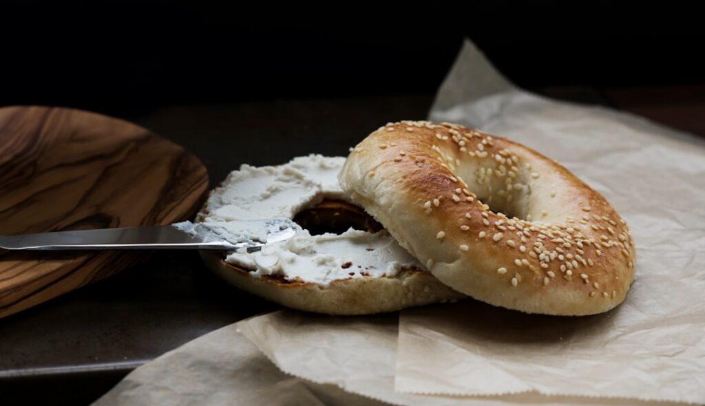 A clean modern shot of a toasted bagel slice spread with creamy white cream cheese generously topped with thinly sliced 