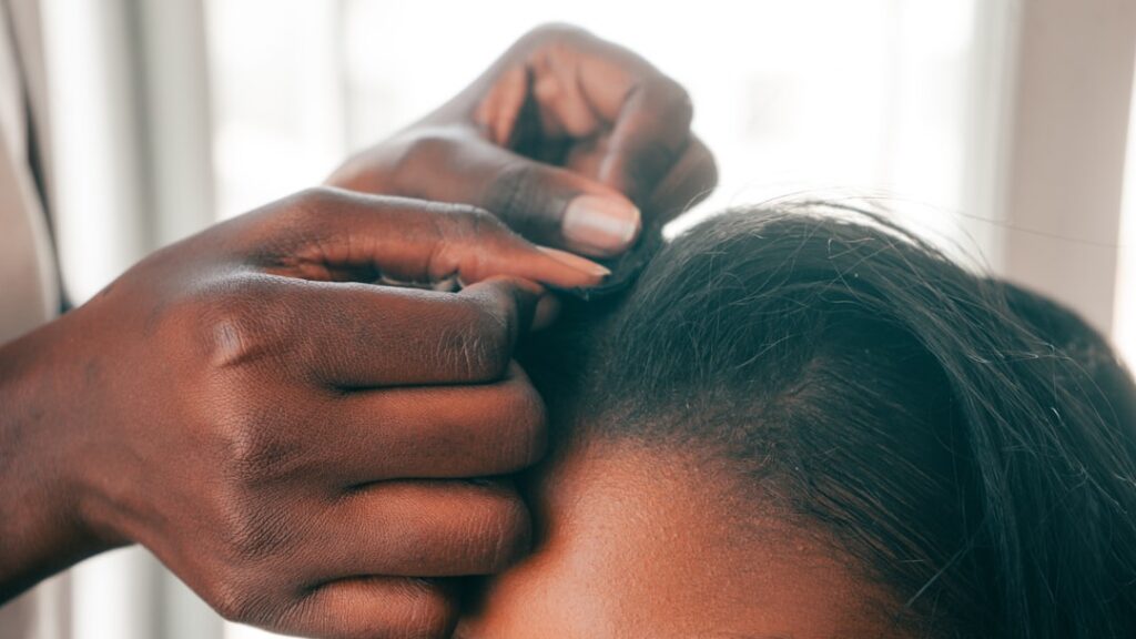 A woman gently massaging a natural hair oil into her scalp with her fingertips showing a focused and self-care moment