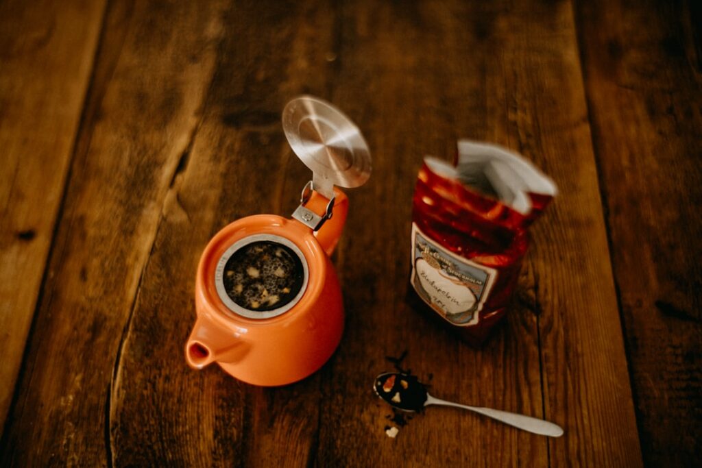 A cup of green Moringa tea with fresh Moringa leaves next to it on a wooden table