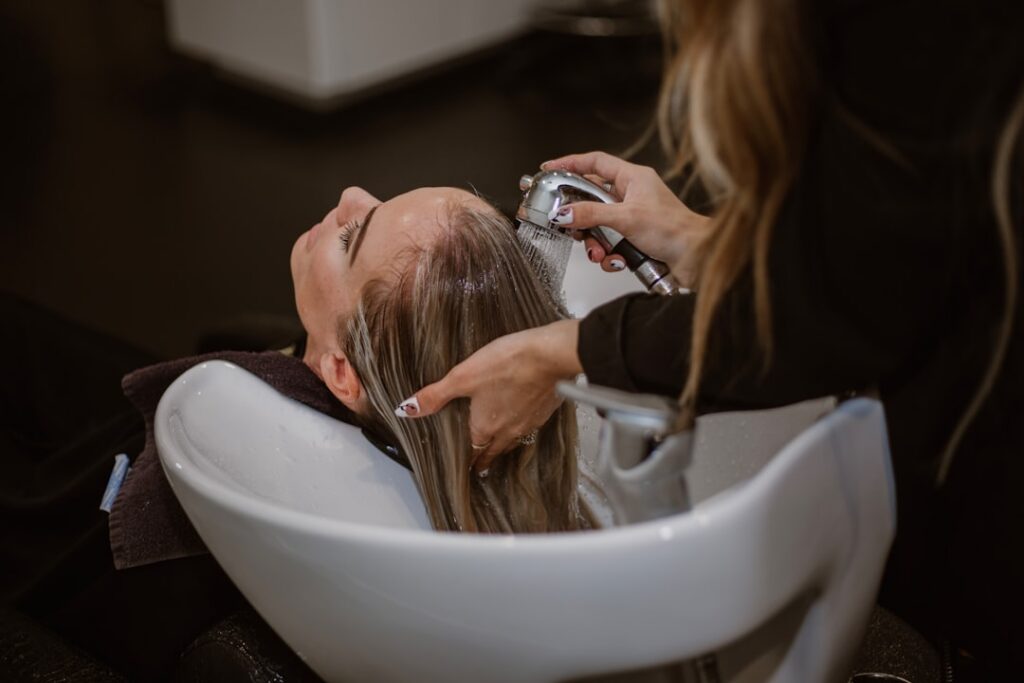 A person gently massaging a clear amber-colored hair tonic into their scalp with fingertips showing healthy shiny hair F