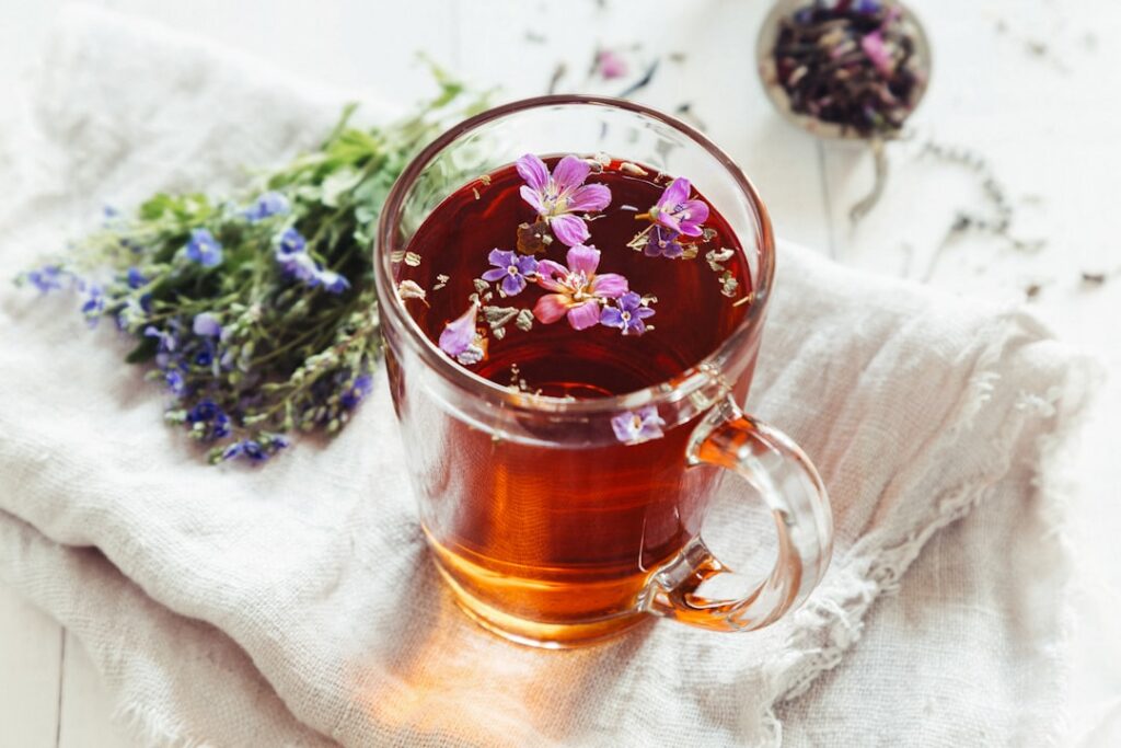 A cup of freshly brewed Yarrow tea golden-green in color with steam rising next to a small bowl of dried Yarrow leaves a