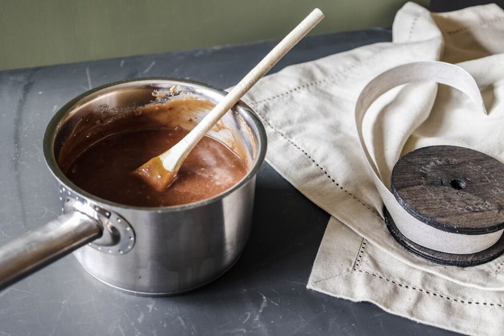 A close-up of a small saucepan on a stove with carob powder being whisked into a liquid to form a smooth paste