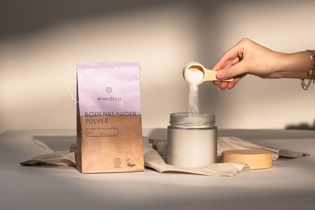 A steaming mug of carob soothing tonic on a wooden table with a few whole carob pods and a small bowl of carob powder ne