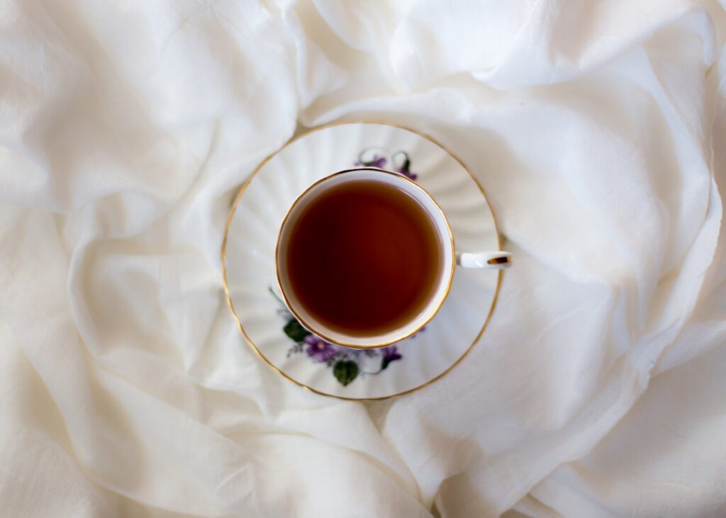 A steaming cup of golden-green Indian Borage tea with a few fresh leaves artfully placed beside it on a rustic wooden ta