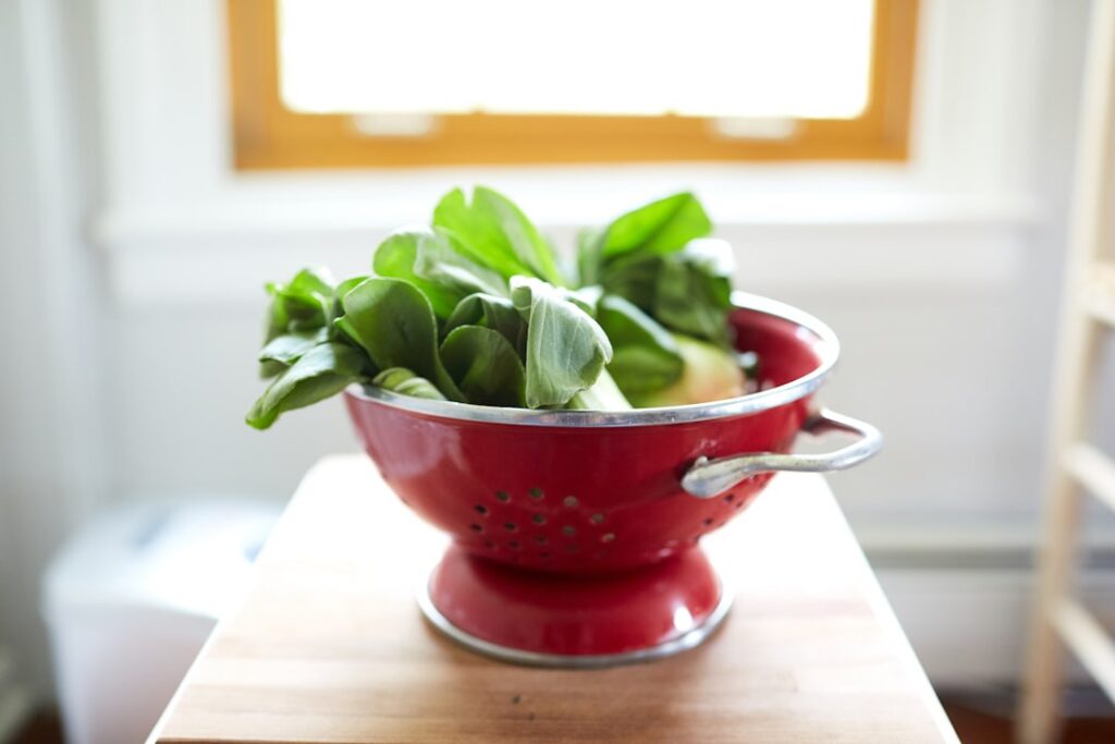 Close-up of fresh purslane leaves and stems in a colander under running water being washed thoroughly