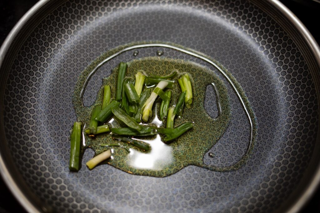 A double boiler setup with a small pot or ladle containing carrier oil and fenugreek seeds gently simmering showing the 