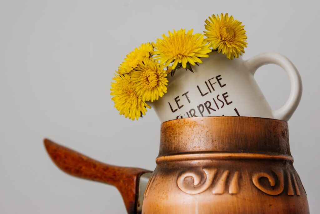 A clear glass mug of warm dandelion tea with a fresh dandelion flower garnish on a rustic wooden coaster
