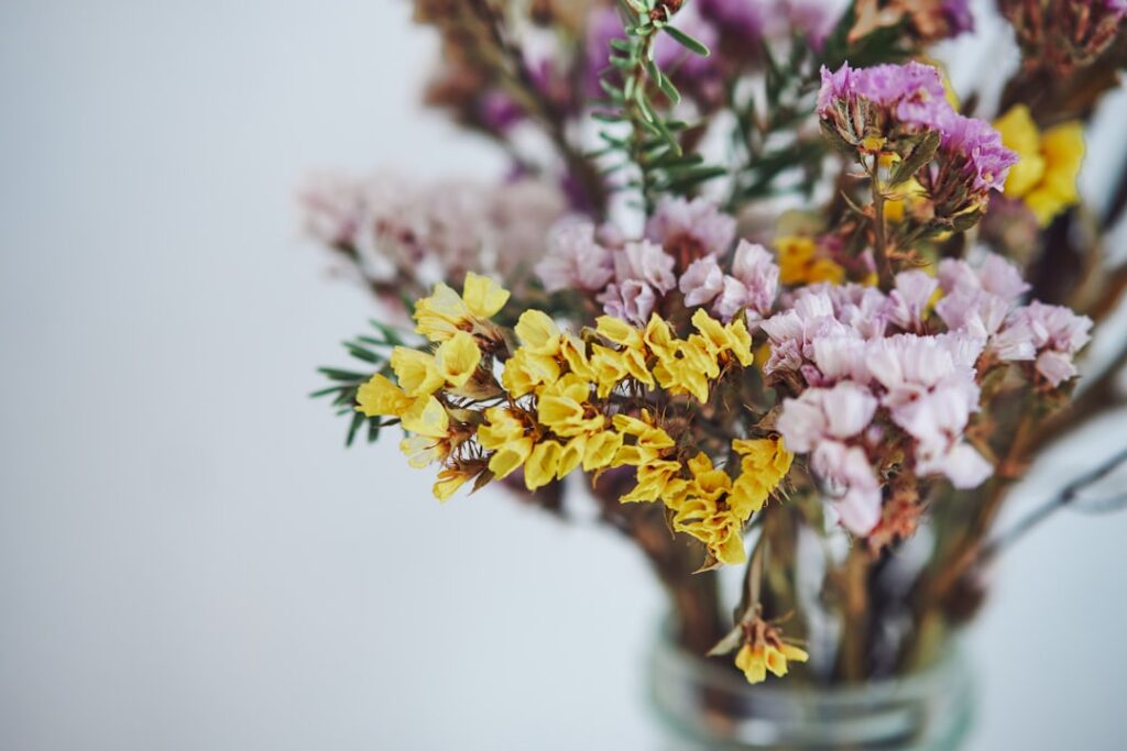 Dried pink Mimosa flowers stored in a clear labeled glass jar placed on a wooden shelf with other herbal ingredients The