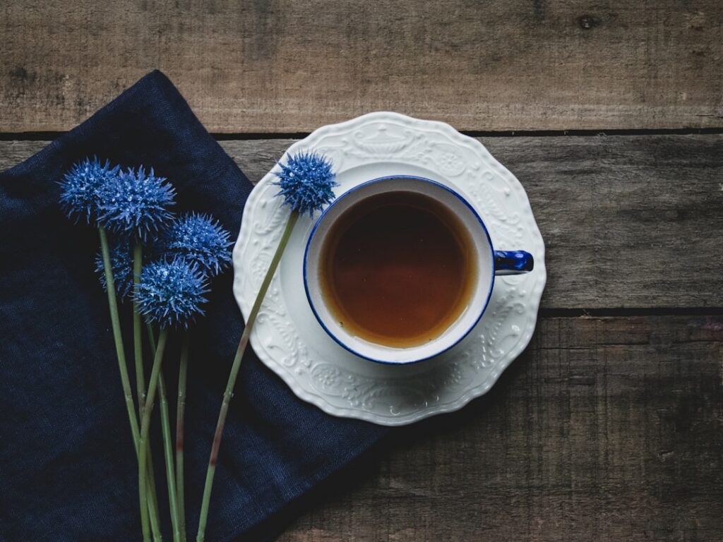A steaming cup of Mimosa flower tea with a few fresh Mimosa blossoms floating on the surface and scattered around the cu