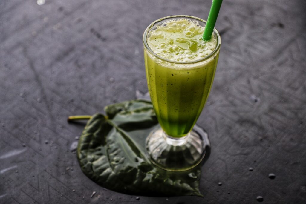 A close-up of a vibrant green liquid freshly strained papaya leaf juice in a clear glass with some leaf pulp on the side
