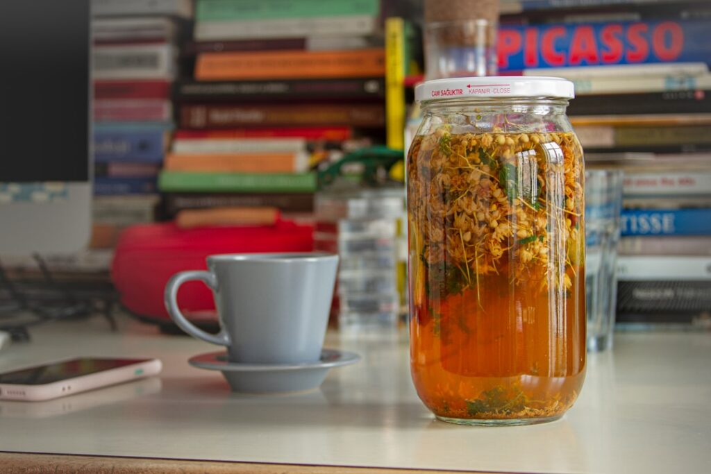 A clear glass jar filled with dried mullein leaves and yellow flowers labeled for storage