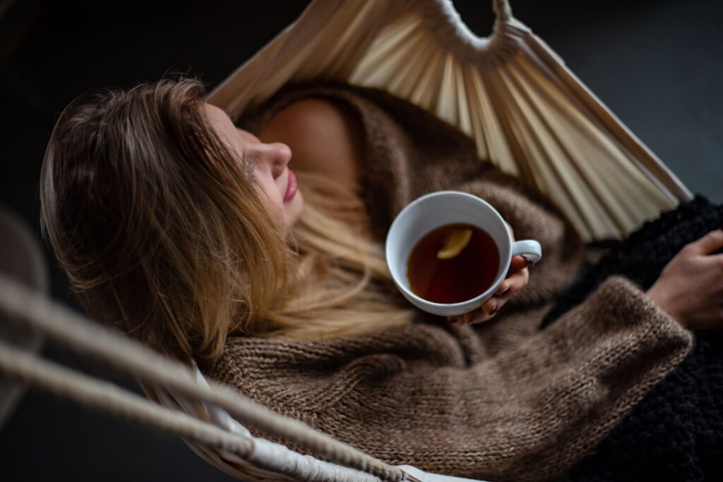 A woman smiling and holding a warm cup of herbal tea looking refreshed and healthy in a cozy kitchen setting