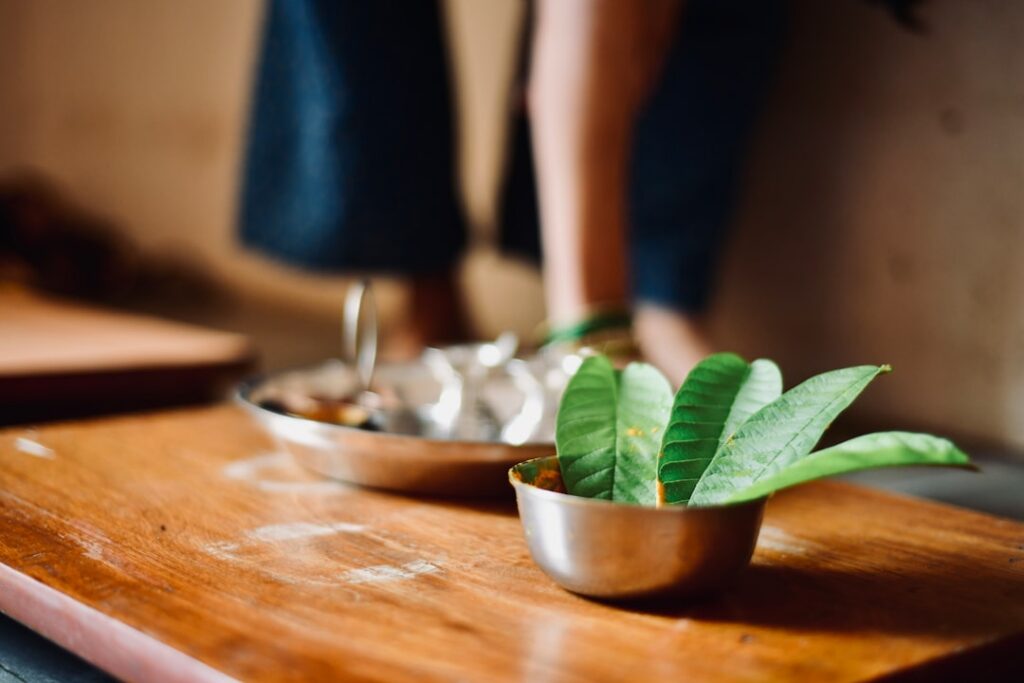A steaming cup of guava leaf tea on a wooden board with several fresh guava leaves beside it suggesting a comforting and