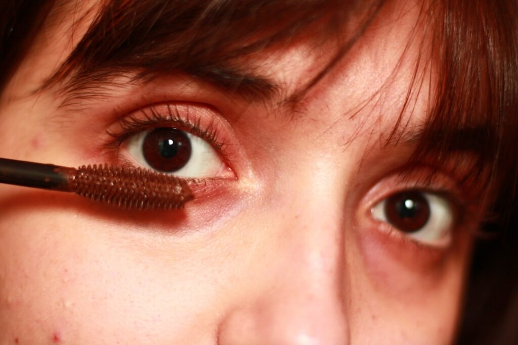 Close-up of a woman s hand gently applying DIY lash serum to her eyelashes using a clean mascara wand Her eye is closed 