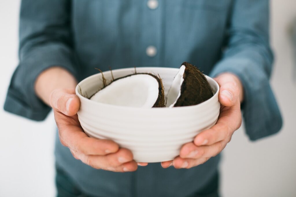 A pair of hands gently holding a wooden bowl filled with a green creamy natural hair mask The background is soft and nat