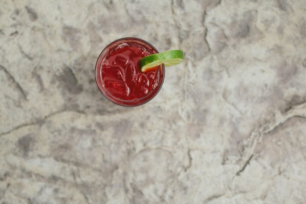 A vibrant red glass of freshly made beet lime ginger and garlic juice being held by a hand