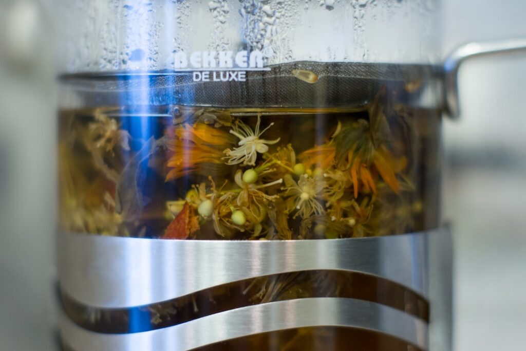 A close-up of a glass mug filled with a golden basil flower infusion steam gently rising with a few fresh basil flowers 