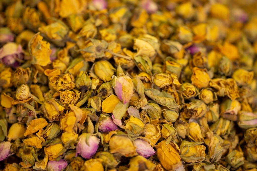 A close-up of dried chamomile flowers showing their delicate petals and yellow centers scattered on a wooden surface