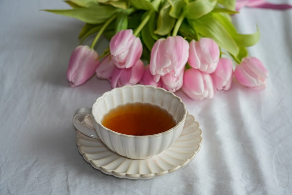 A clear glass teacup filled with golden lavender infusion with a few lavender buds at the bottom and a wisp of steam ris