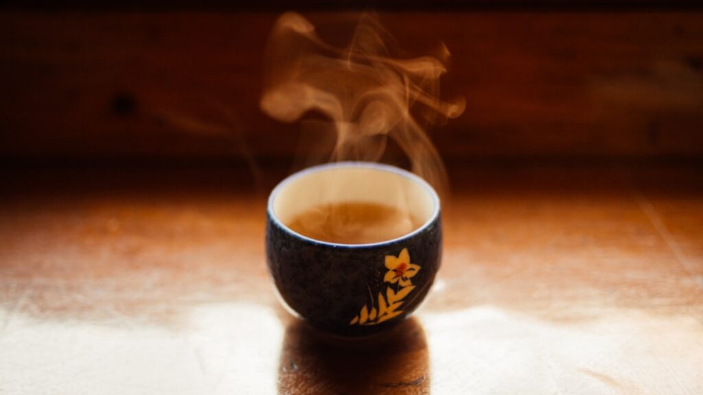 A steaming cup of freshly brewed guava leaf tea on a rustic wooden table with some whole guava leaves blurred in the bac