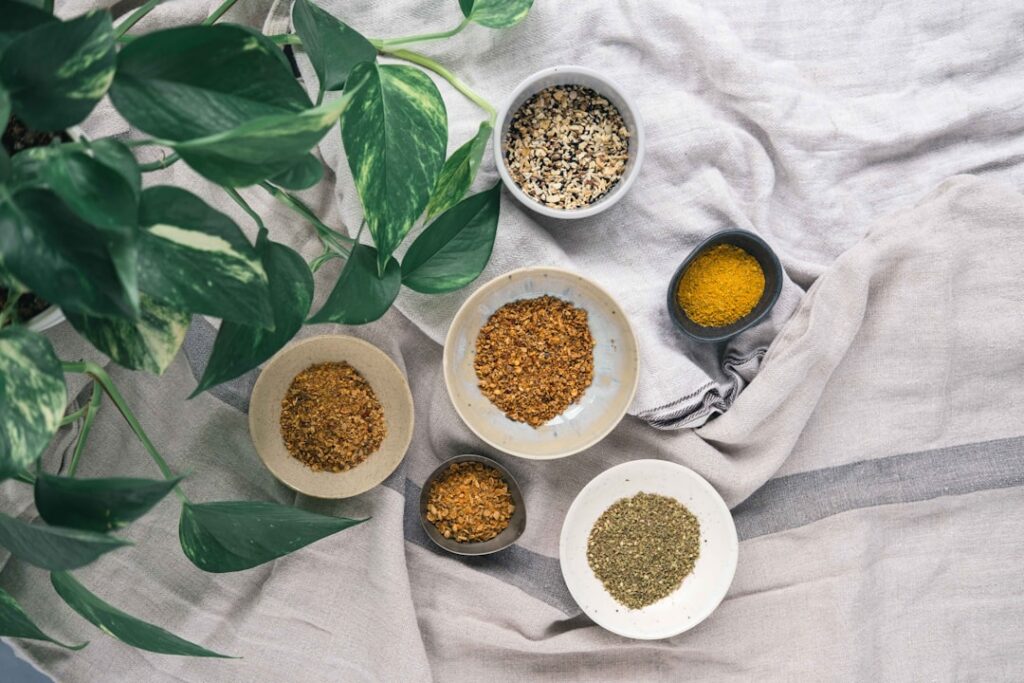 Close-up of bowls containing flax seeds and white rice on a wooden surface with whole cloves scattered around ready for