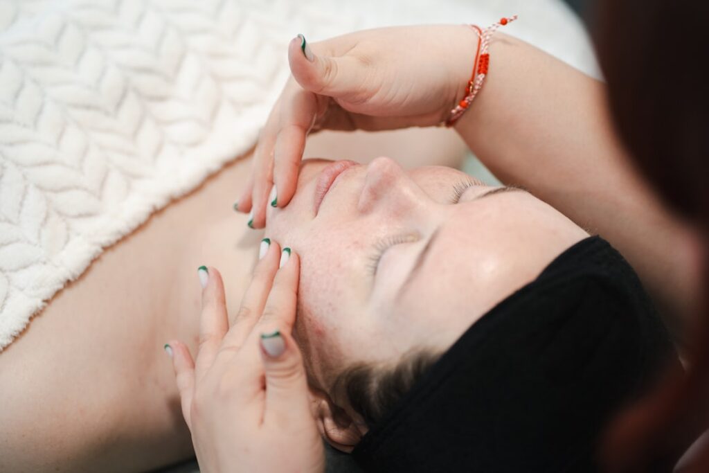 A woman gently massaging a few drops of natural oil onto her face and neck in an upward motion with a soft glowing compl