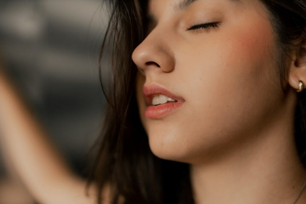 A woman gently touching her remarkably smooth radiant and youthful-looking face with her eyes closed showcasing soft dew