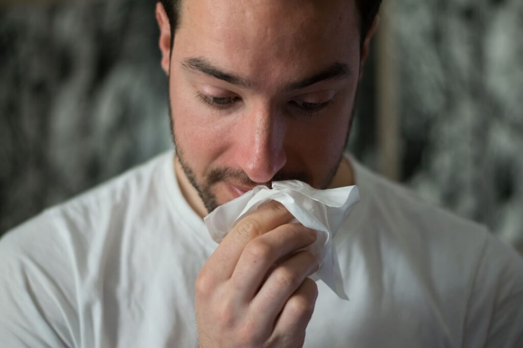 Person gently blowing their nose into a tissue looking thoughtful about their health