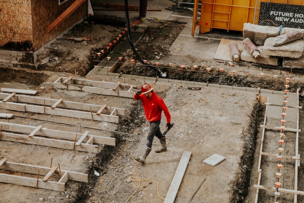A close-up image showing a gardener inspecting the concrete foundation and wooden base of an old shed for cracks rot or