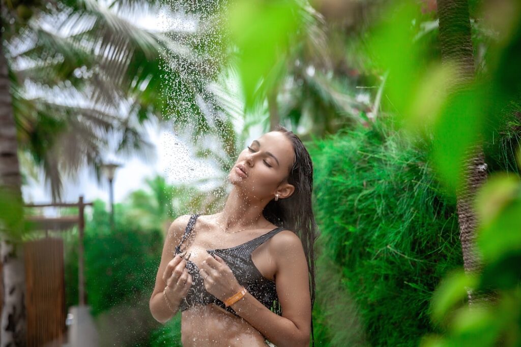 A woman gently pouring rice water over her hair in the shower as a rinse demonstrating the application method