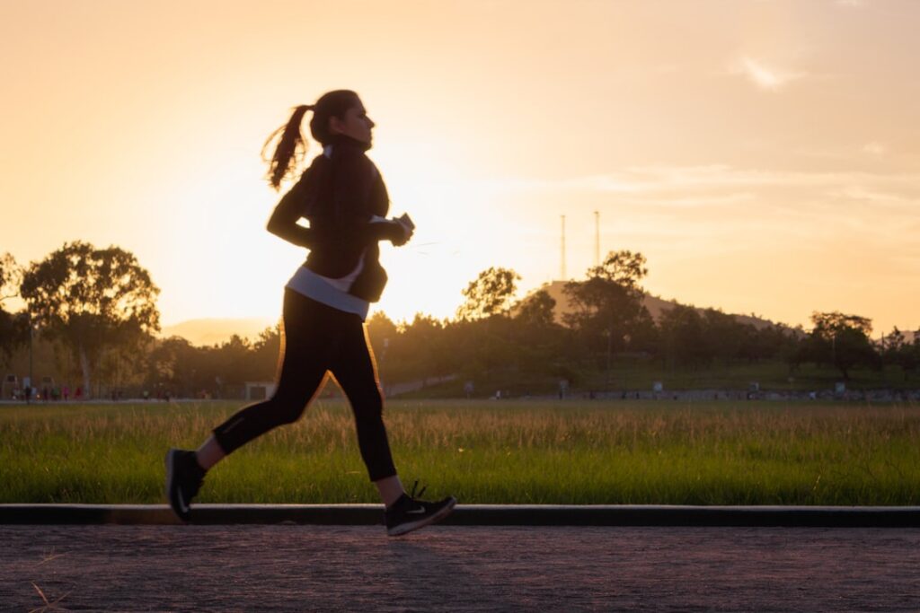 A person smiling and running outdoors in the sunshine illustrating the benefits of exercise and sunlight for happy hormo